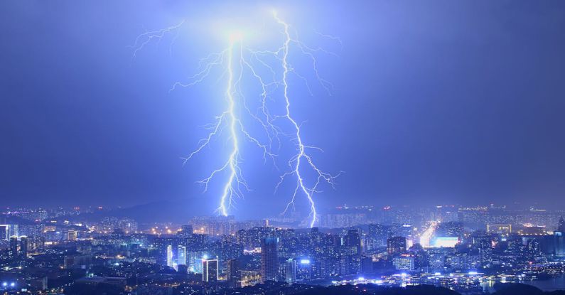 Energy Infrastructure - Breathtaking thunderstorm with lightning bolts over modern illuminated city at night with purple sky
