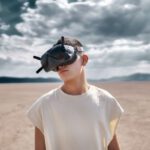 Drones Inspection - man in white crew neck t-shirt wearing black sunglasses standing on brown sand during daytime